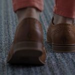 Shoes of a person walking on a gray carpet