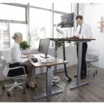 A female worker seated and male worker standing at height-adjustable desks