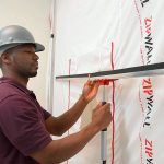 Worker raising the ZipWall FoamRail Span Adjustable Tapeless Seal up a dust barrier to seal off a work area