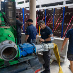 Facilities team working on pumps (large green machine), with AquaFence barrier in background