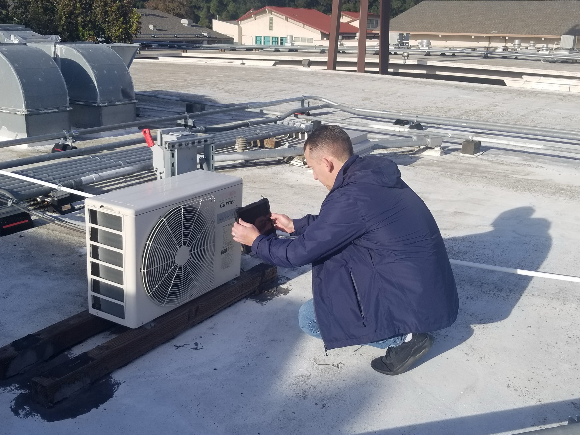 FM technician kneeling on a roof to take an image of HVAC equipment with his tablet