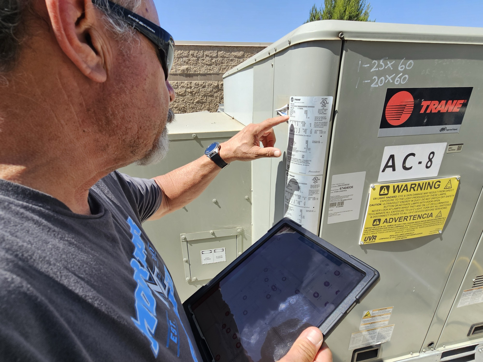 An FM technician checking TRANE HVAC equipment, holding a tablet