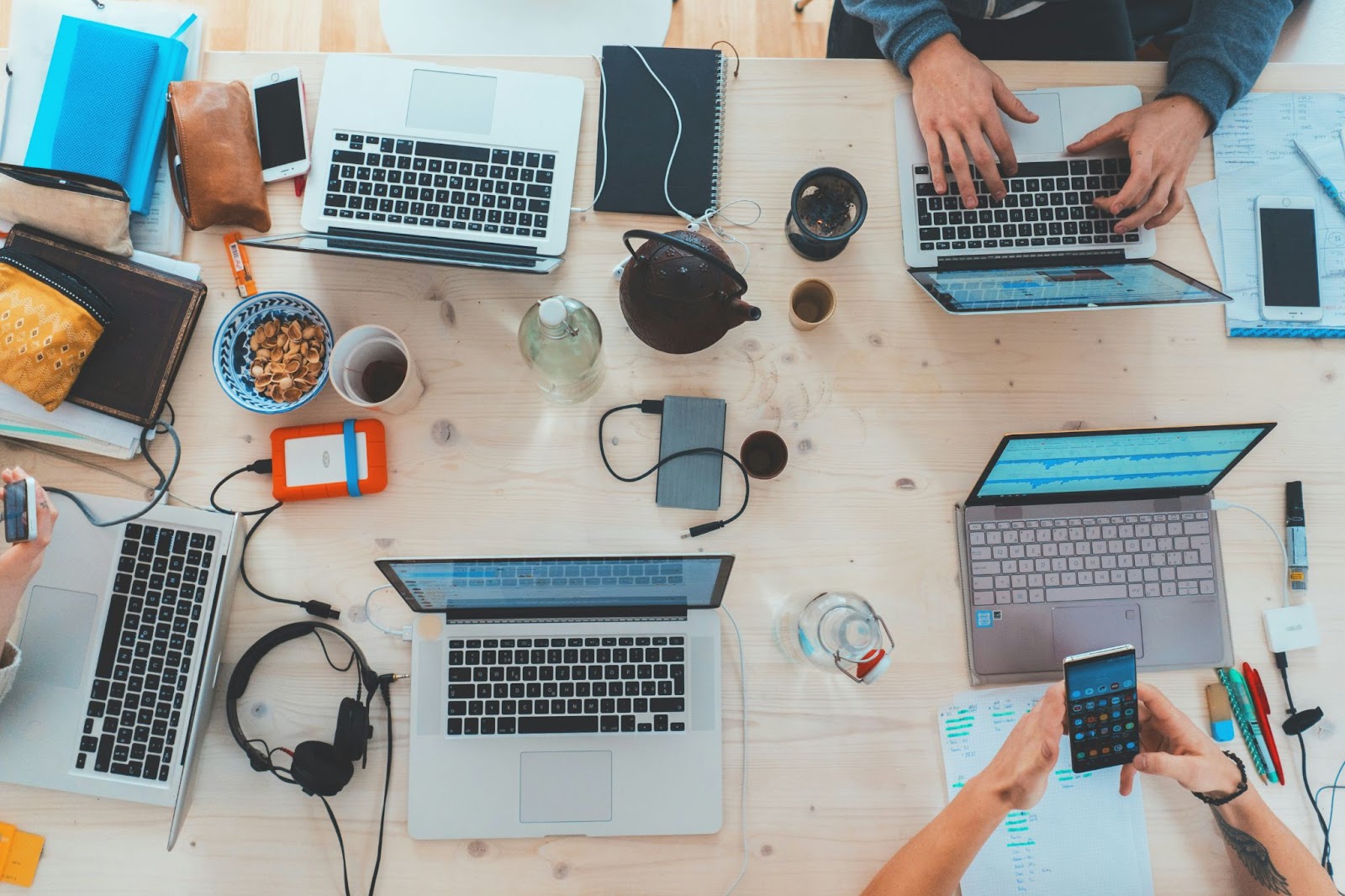 Overhead view of people working on laptops, with accessories, to illustrate digital-led maintenance