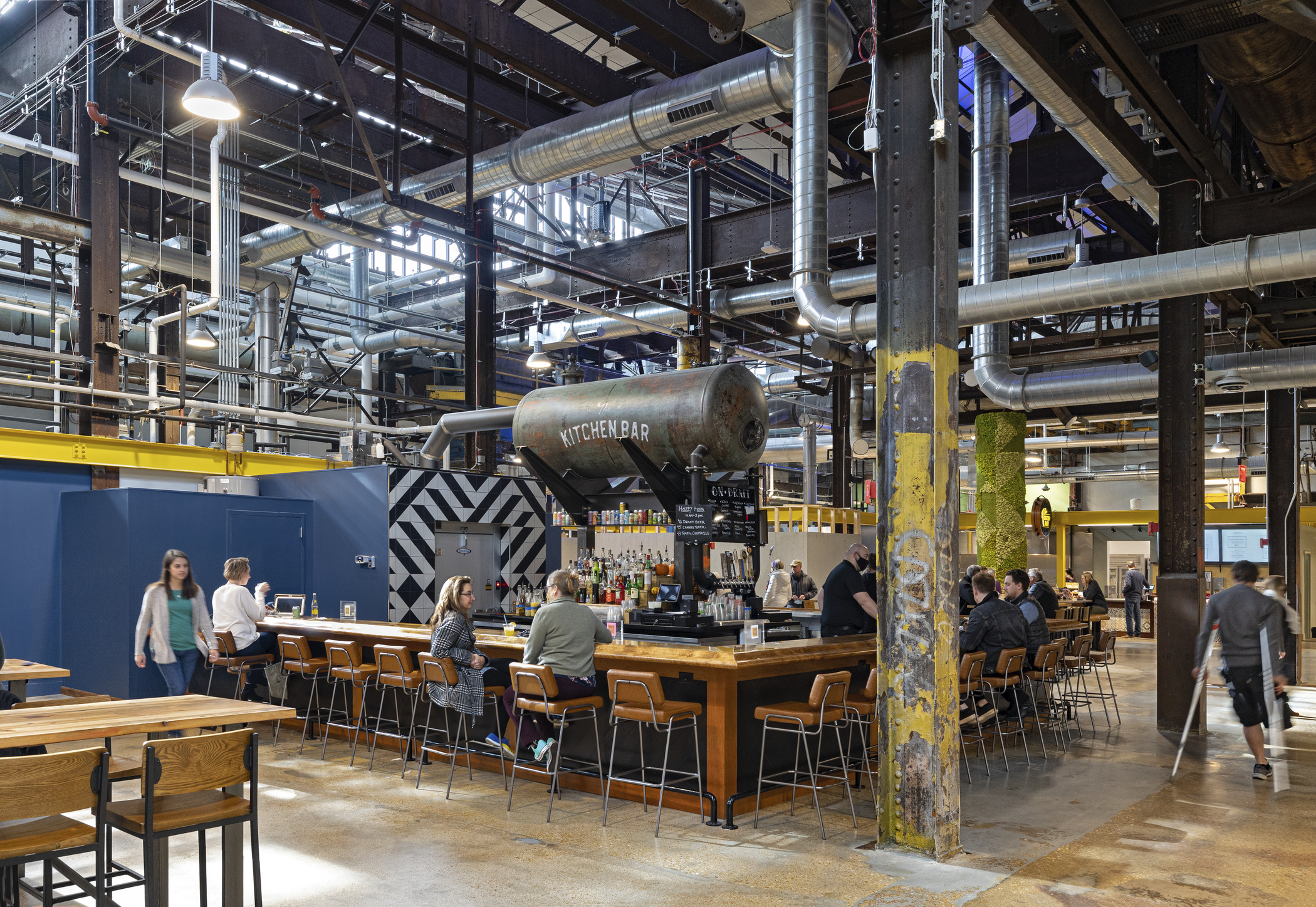 The Food Hall at City Foundry STL, with people seated at a long wooden bar, and pipes and beams visible - example of adaptive reuse