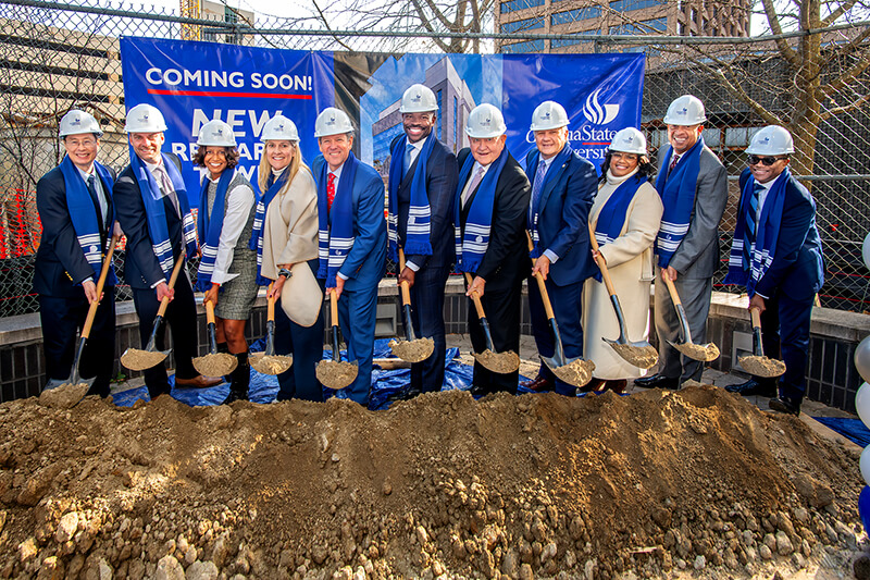 GSU and state officials in hard hats and blue GSU scarves hold shovels with dirt at groundbreaking of Research Tower