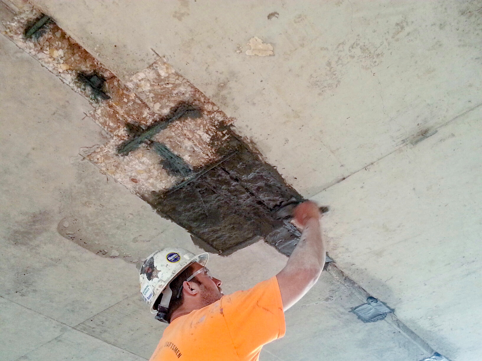 WSC worker in orange shirt and hard hat repairing parking structure ceiling